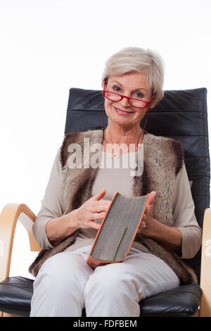 smiling senior old woman reading book in chair Stock Photo