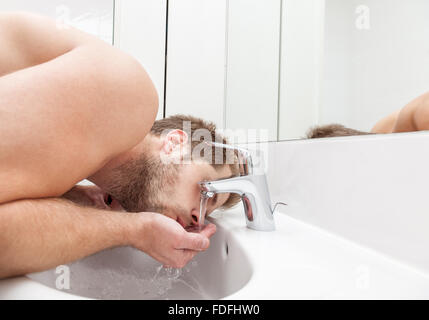 Man drinks tap water from the bathroom sink Stock Photo