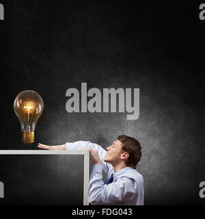 Young man looking from under table at glass light bulb Stock Photo