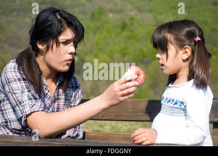 Teenage girl offering an apple to little sister Stock Photo