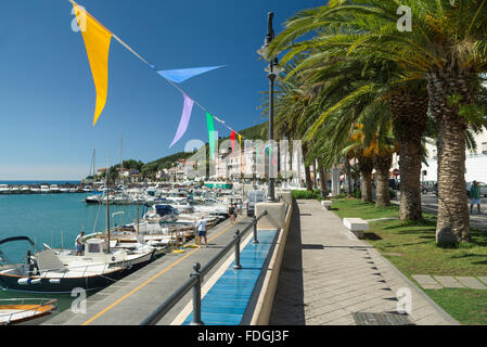 Colorful pennants and palm trees on the harbor promenade in picturesque town of Scario on the coast of Cilento, Campania, Italy Stock Photo