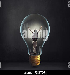 Cheerful girl inside of glass light bulb on dark background Stock Photo