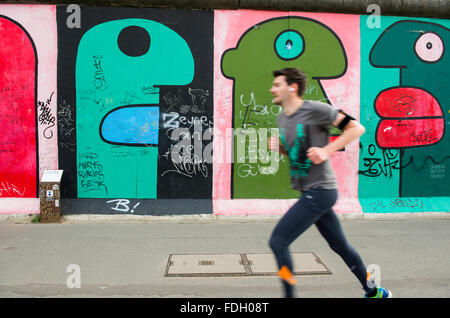 Male jogger running past artwork on the Berlin Wall at the East Side Gallery in the German capital city Stock Photo
