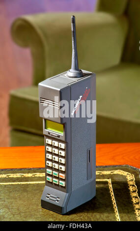 1980s MOBIRA CITYMAN OLD MOBILE PHONE 1987 first generation hand held mobile cell phone Nokia Mobira Cityman 1320 on desk with 1980's armchair behind Stock Photo