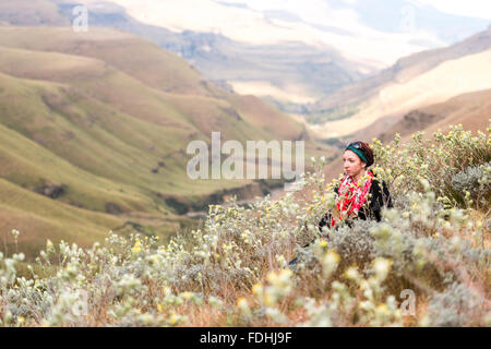 Young woman sitting amongst the wildflowers with rolling hills in the background in Sani Pass, between South Africa and Lesotho. Stock Photo