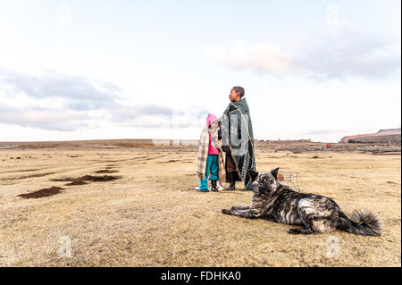 Children wrapped in blankets, standing with their dog on a vast plane in Sani Pass, Lesotho, Africa Stock Photo