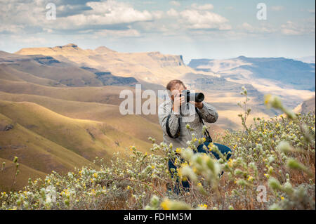 Man taking photographs while standing amongst the wildflowers with rolling hills in the background in Sani Pass, between South A Stock Photo