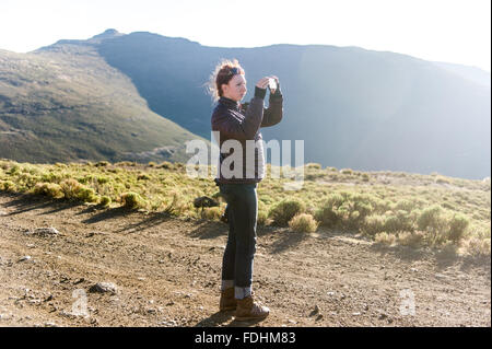 Young woman taking a photo with her cell phone in the mountains of Lesotho, Africa Stock Photo