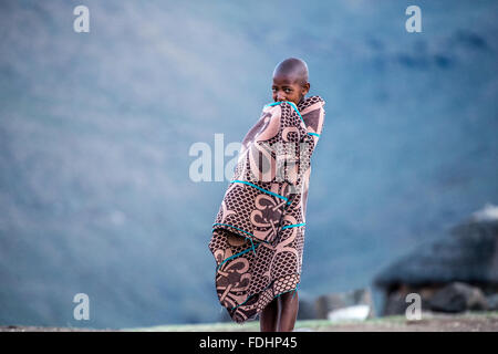 Young boy wrapped in a blanket standing in front of a mountain range in Lesotho, Africa Stock Photo