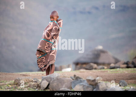 Young boy wrapped in a blanket standing in front of a mountain range in Lesotho, Africa Stock Photo