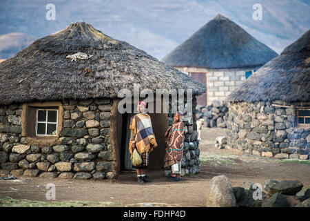 Local children wrapped in blankets standing in front of village huts in Lesotho, Africa Stock Photo