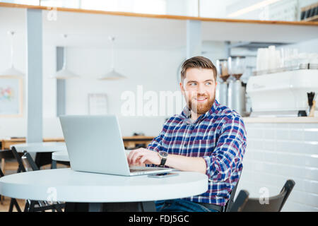 Smiling young man using laptop computer and looking away in coffee shop Stock Photo