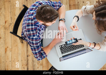 Top view of young couple sitting at round table and using laptop and cell phone Stock Photo