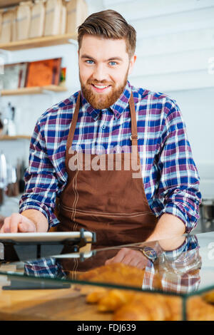 Potrait of attractive happy bearded barista in brown apron at work in coffe shop Stock Photo