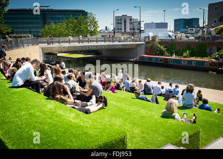 Crowd enjoying sunny afternoon sitting on artificial turf by Regent's Canal, King's Cross, London, UK Stock Photo