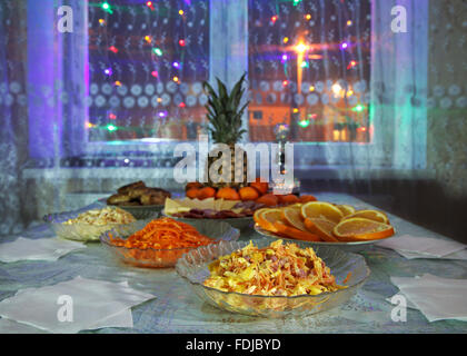 festively laid table with salads, pineapple, meat, wine and  tangerines at night Stock Photo
