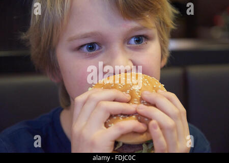 Child blond boy eats hamburger in fastfood Stock Photo