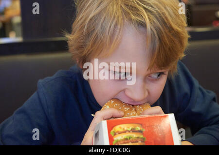 Child blond boy eats hamburger in fastfood Stock Photo