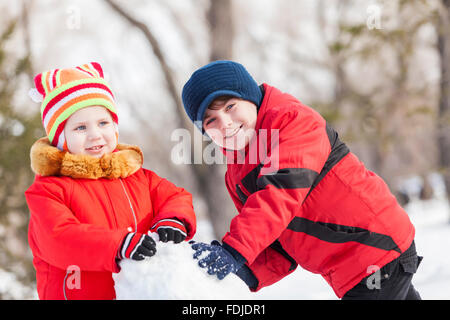 Cute boy and girl building snowman in winter park Stock Photo