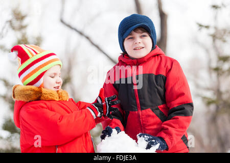 Cute boy and girl building snowman in winter park Stock Photo