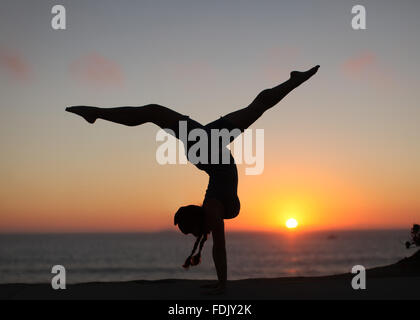 Silhouette of a Woman doing handstand with legs apart on the beach Stock Photo