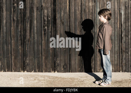 Boy standing next to a wooden fence with alter ego shadow Stock Photo