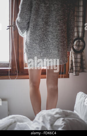 Rear view of a woman standing on bed looking out of the window Stock Photo