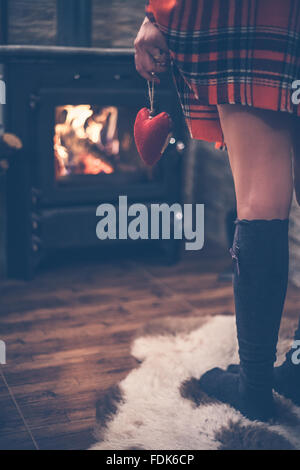 Rear view of a woman standing in front of wood burning stove holding red heart in her hand Stock Photo