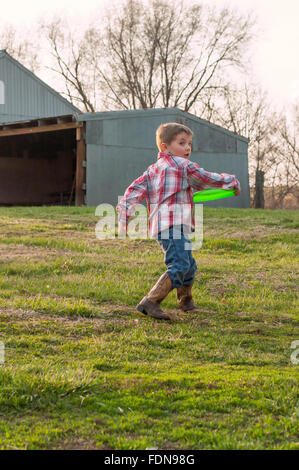 Boy wearing boots throwing frisbee on farm Stock Photo