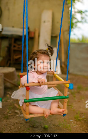 Beautiful baby sitting on wooden swing Stock Photo