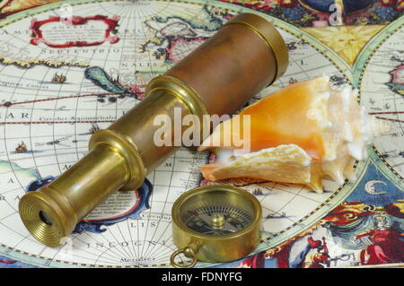 Old spyglass, compass and seashell lying on the vintage map of the world. Stock Photo