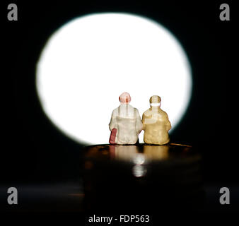 Miniature figurine pensioners sitting on coins in front of a blank spotlight Stock Photo