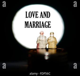 Miniature figurine pensioners sitting on coins in front of a spotlight showing the words Love and marriage concept Stock Photo