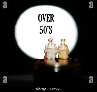 Miniature figurine pensioners sitting on coins in front of a spotlight showing the words over 50's concept Stock Photo