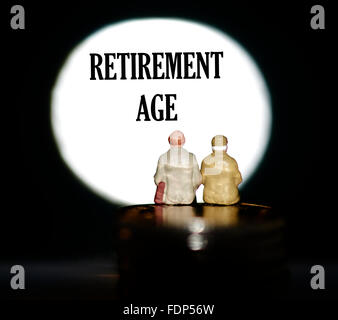 Miniature figurine pensioners sitting on coins in front of a spotlight showing the words Retirement age concept Stock Photo