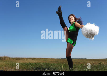 Young cheerleader in green costume jumping against blue sky Stock Photo