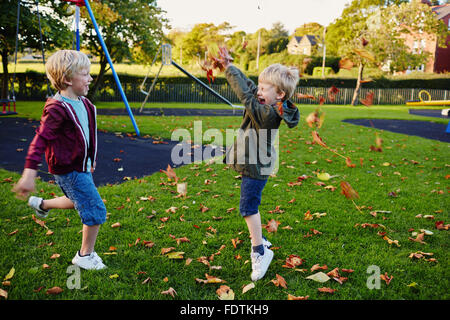 Two young boys throwing leaves in the park having fun. Stock Photo