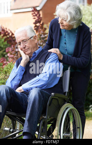 Depressed Senior Man In Wheelchair Being Pushed By Wife Stock Photo