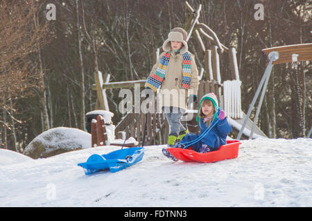 Young brother and sister sledging down hill in Neverland Play Park, Kirriemuir, Scotland, 2016 Stock Photo