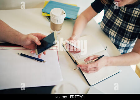 Two students using their smart phones whilst studying. Stock Photo