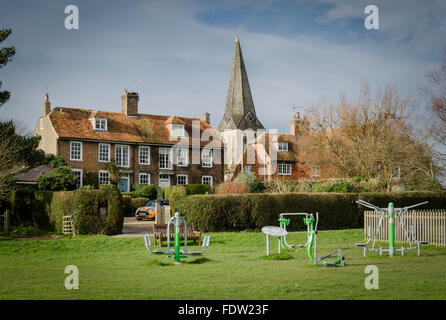 Exercise equipment on Woodchurch village green, Kent, UK, with All Saints church and brick and tiled cottages in the background Stock Photo