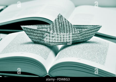 closeup of a paper boat, made with a printed paper with non-sense words, on an open book, in black and white