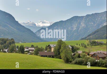 Idyllic landscape in the Alps with fresh green meadow, village and high mountain tops in the background snow covered. Austria. Stock Photo