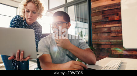 Portrait of young team of graphic designers working together in a new project, with woman showing something important to a colle Stock Photo