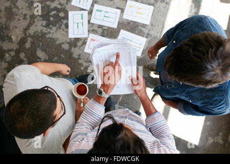 Top view of hands of three young people discussing financial transactions during a meeting. Man pointing at document while stand Stock Photo