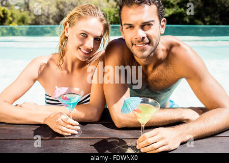 Happy couple leaning on pool edge and holding cocktails Stock Photo