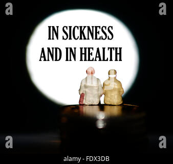 Miniature figurine pensioners sitting on coins in front of a spotlight showing the words In sickness and health concept Stock Photo