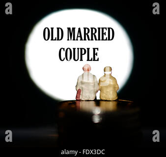 Miniature figurine pensioners sitting on coins in front of a spotlight showing the words Old married couple Stock Photo
