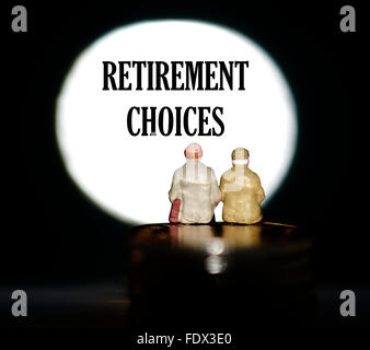 Miniature figurine pensioners sitting on coins in front of a spotlight showing the words Retirement choices Stock Photo