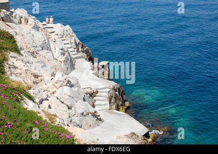 Rocky beach with stairs and sunbathing couple in Hydra, Greece Stock Photo